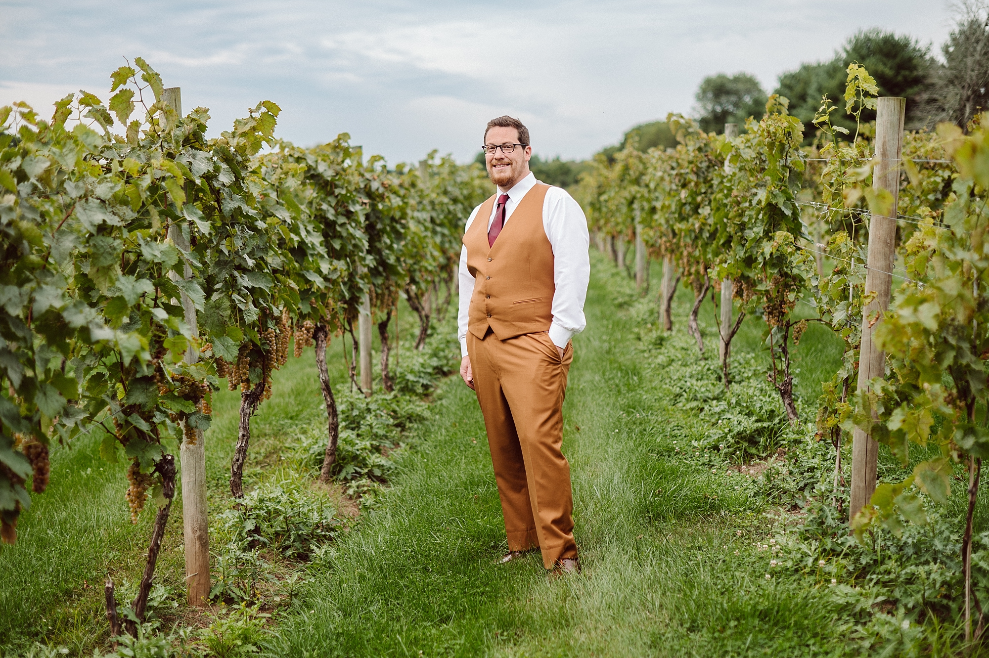 groom poses in vineyard grapes 