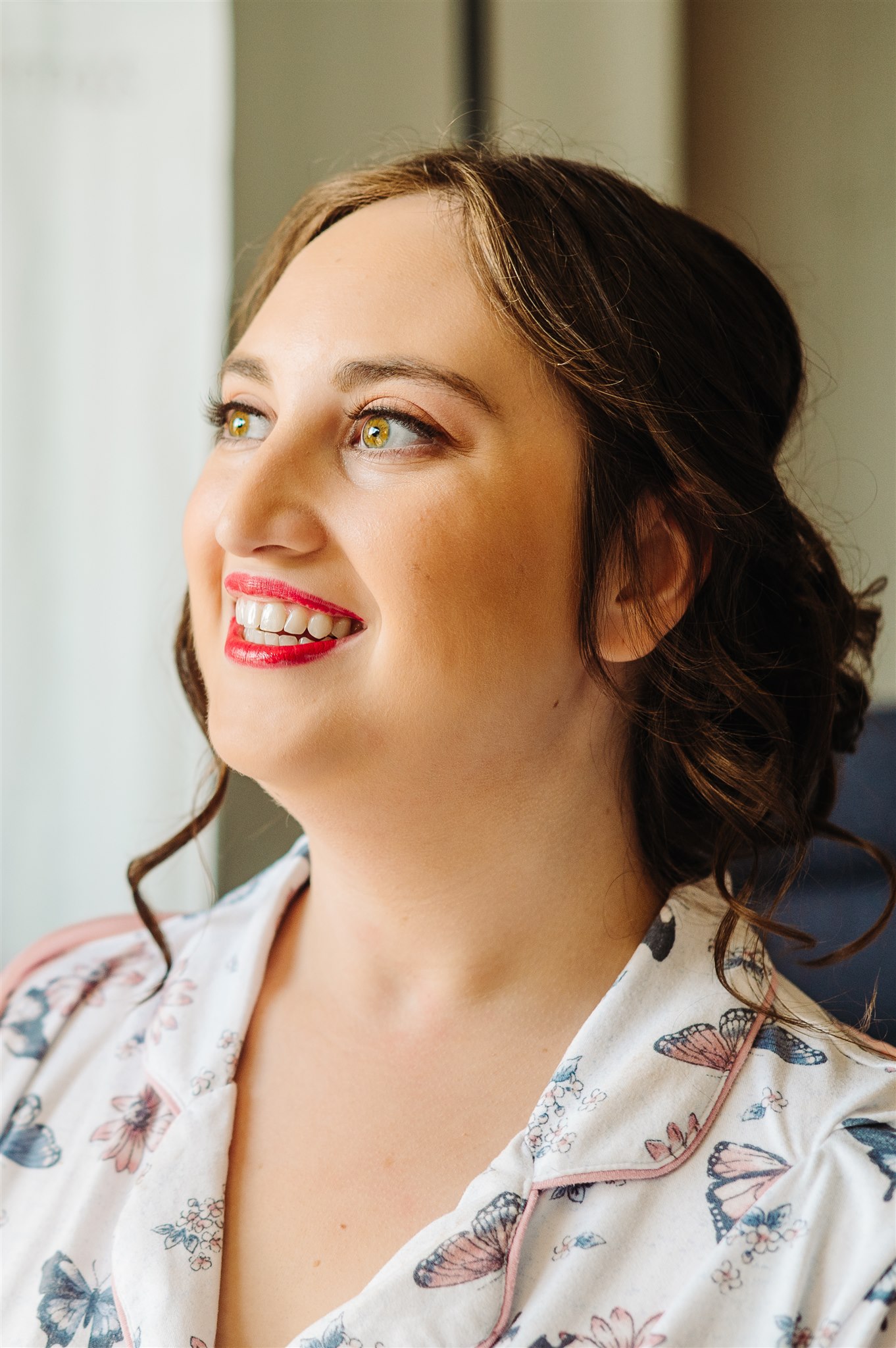 Woman with brown hair and pink lipstick smiling, wearing white top with butterfly pattern.