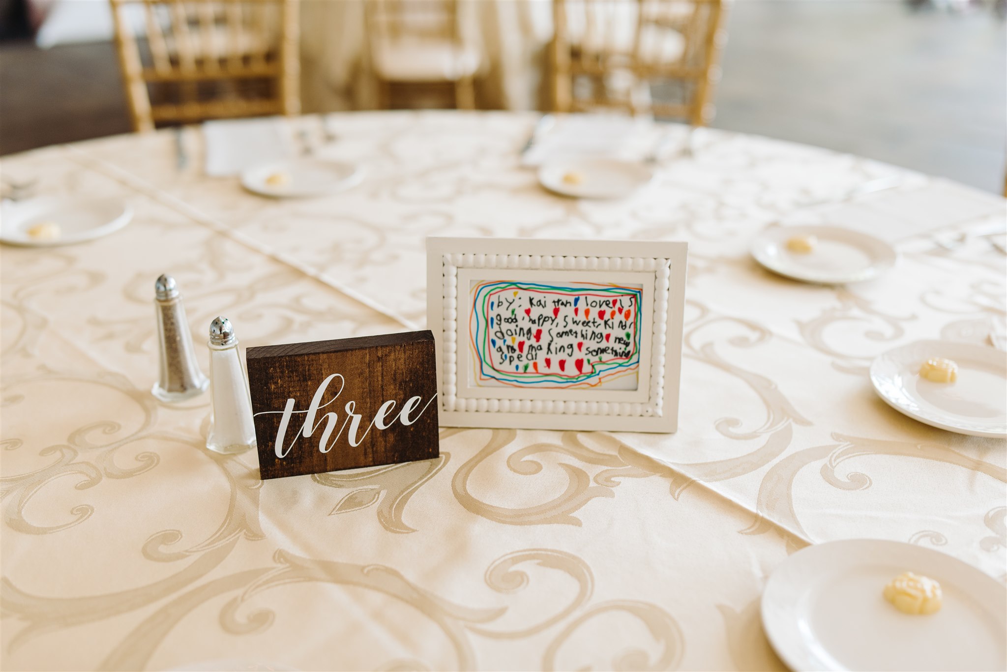 Round table with table number "three," handwritten message, plates with butter, salt and pepper shakers.