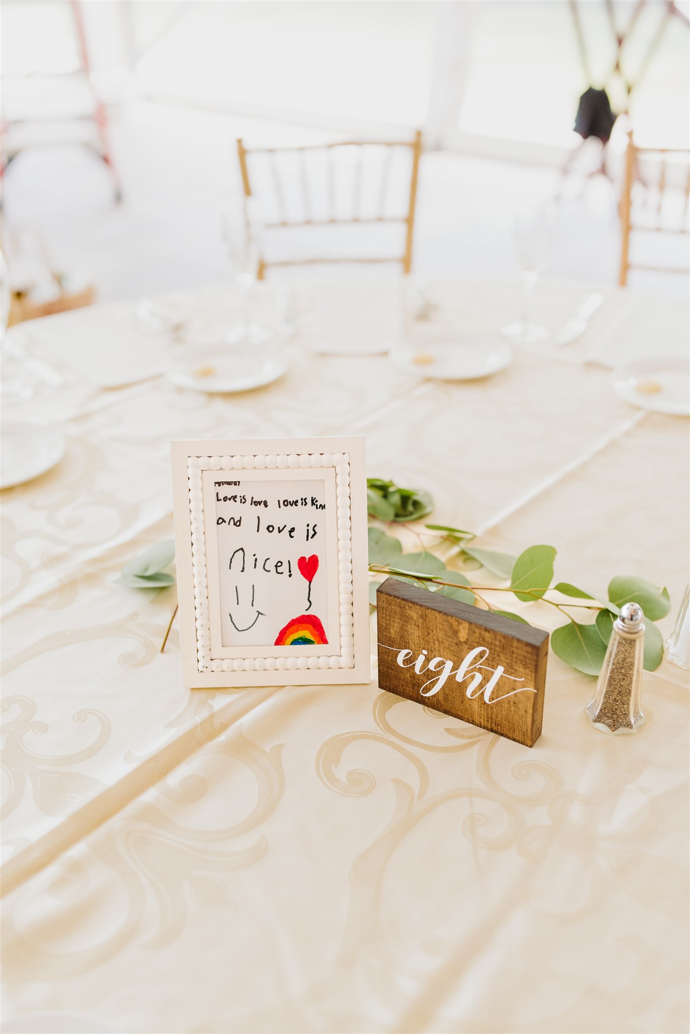 Wedding reception table with framed hand-drawn message, table number "eight", and light decor.