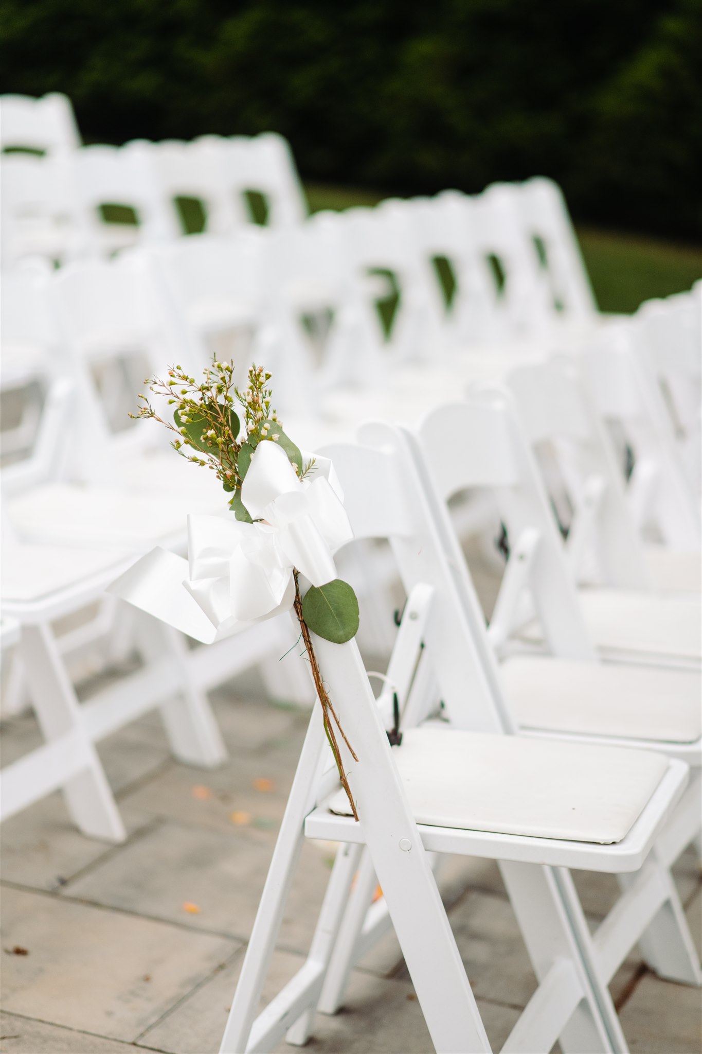 White folding chairs in rows; one decorated with a small flower bouquet and white ribbon.