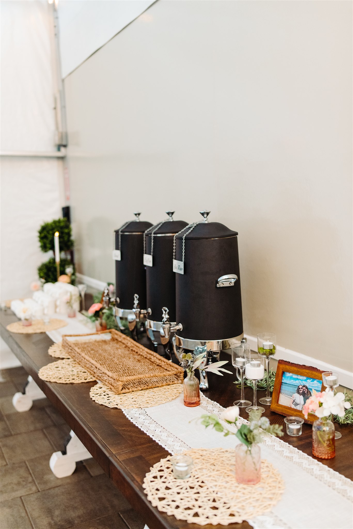 Neatly arranged table with three black dispensers, wicker mats, glass candles, flowers, and framed photo.