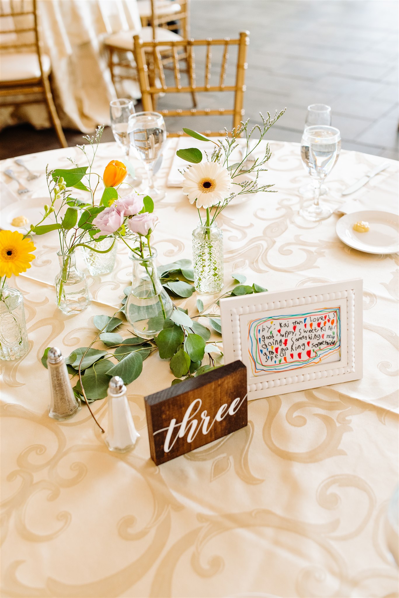 Elegantly set banquet table with flowers, handwritten note, number three, and dinnerware.