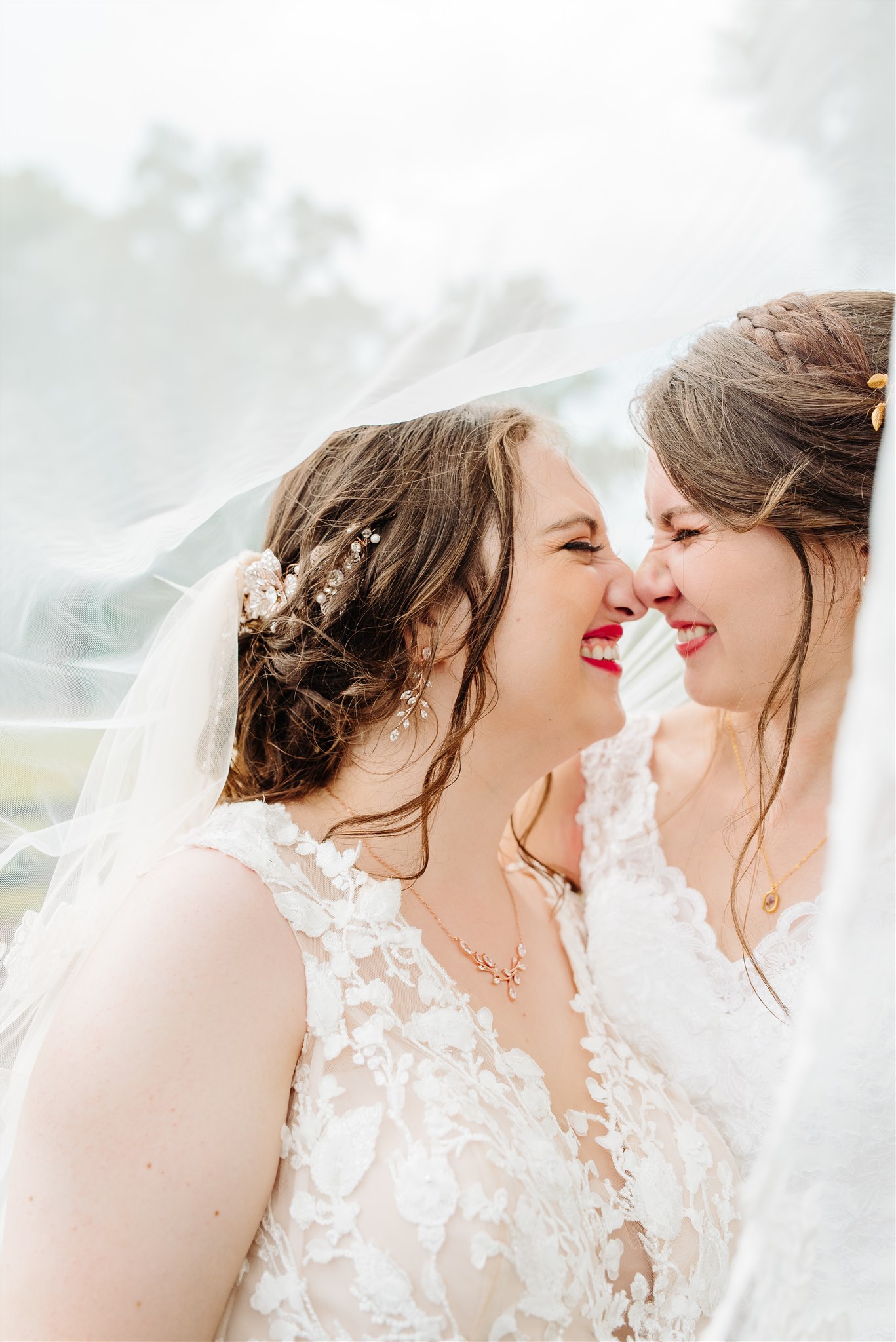 Two women in white dresses sharing an intimate moment, smiling and touching noses.